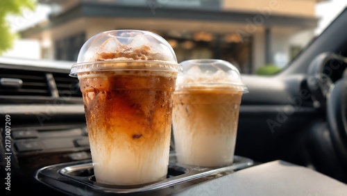 Takeaway iced coffee drinks in car cup holder with clear cups, milk layers and condensation for modern drive through cafe marketing and beverage branding