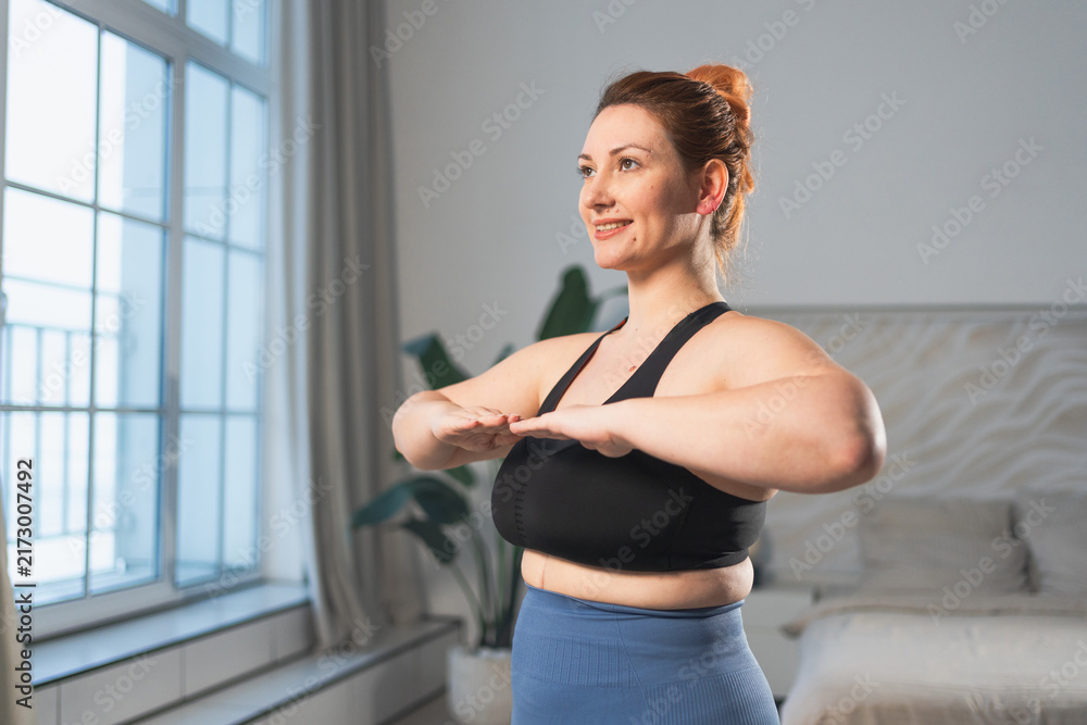 Fototapeta premium Fitness workout training. Woman practicing fitness at home. Plus size female doing sports exercise at home indoor. Girl in sportswear have workout weight training for weight loss. Sport and fitness