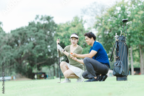 Cuadro en lienzo Asian couple learning golf on a green course, man coaching woman on putting tech