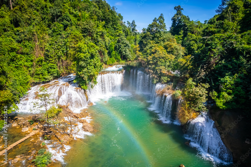 Fototapeta premium Aerial view of vibrant rainbow over turquoise river pool with waterfall cascading in lush green forest at Glue-Thor Waterfall (Kyone Htaw Waterfall), Kayin State, Myanmar.