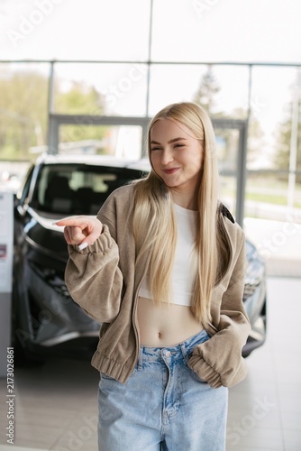 Young woman pointing new car in dealership showroom