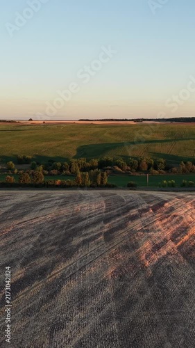 Vertical video. Expansive aerial view of rolling agricultural fields and farmland during a beautiful golden hour sunset, showing cultivated land and green meadows under a clear evening sky