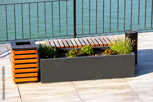 A modern bench with a trash can, ashtray, flower bed, and charger for phones and gadgets.