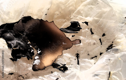 A detailed abstract texture showing severely burned and melted plastic material with dark charred areas, black fragments, scorched marks and translucent fire damaged texture surfaces