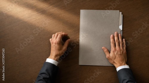 Businessman closing confidential folder with golden seal on wooden table in office