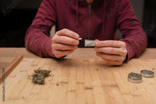 Canvastavla Close up of unrecognizable man putting filter into blunt with dried cannabis lea