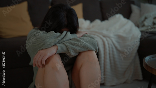 Photography A woman sits on the floor, leaning against a sofa with her knees pulled up, bury
