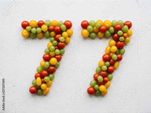 Number 77 formed by fresh cherry tomatoes and grapes on white background