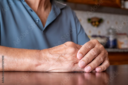 Fotografie Senior person resting hands on a wooden table, displaying the visible signs of a