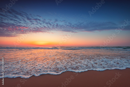 Quadro su tela Scenic sandy beach sunset with white sea foam washing ashore under colorful sky