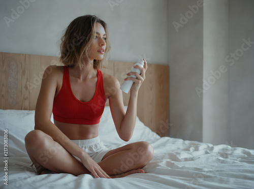 Portrait of a young woman doing her morning routine and spritzing perfume on a bed