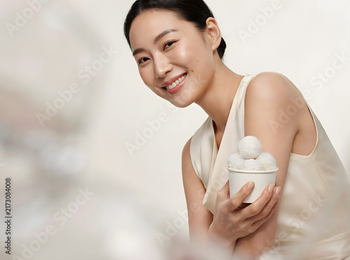Happy young Asian woman presenting a small bowl of wellness products or healthy snacks