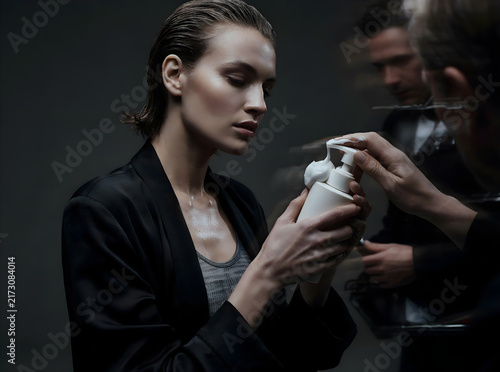 Elegant woman performing a skincare routine with cosmetic products in a dimly lit studio environment