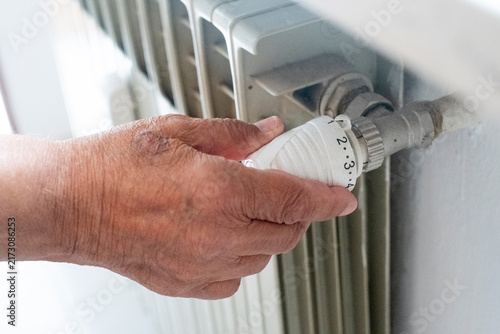 Obraz na płótnie Elderly hand adjusting the thermostatic radiator valve, managing household tempe