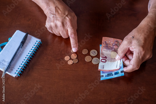 Foto Elderly person's hands counting euro coins and banknotes on a wooden table, mana
