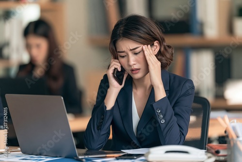 Stressed businesswoman sitting at a desk with a laptop while talking on the phone in an office