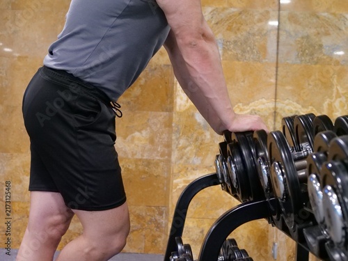 Принти на полотні Close-up of muscular man leaning on a heavy dumbbell rack in gym