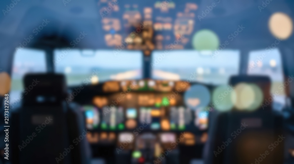 Naklejka premium Airplane cockpit interior view with blurred instrument panel and runway lights. The flight deck displays glowing controls and navigation systems during a low visibility approach.