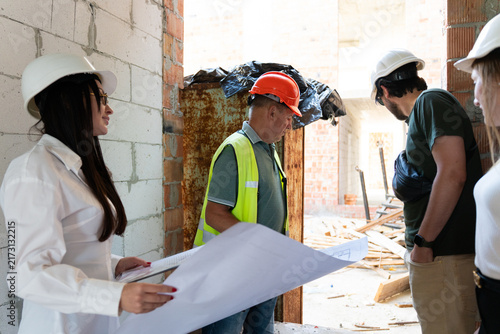 Construction workers in safety vest think about work process uotside. Experienced constructors and lady experts inspect building analyzing process