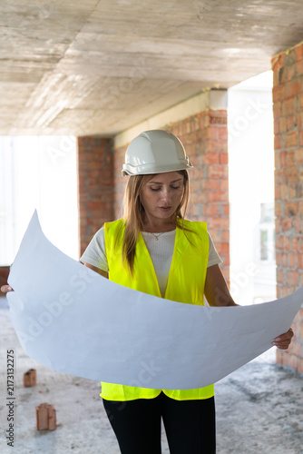 Engineer woman in hard hat holds large blueprint near brick corridor. Specialist studies dimensions verifying section order before work starts