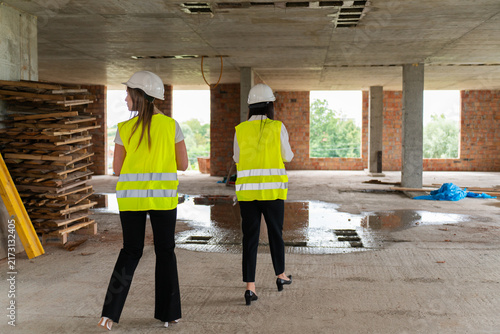 Female engineers inspect work areas during verification process. Women in hard hats and vests analyze results of building assessing project stage