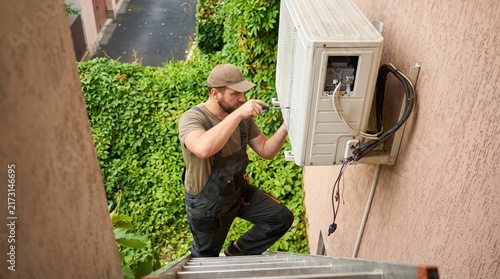 HVAC technician repairing wall mounted air conditioning unit outdoors in residential area