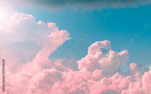 Fluffy pink cumulus clouds filling a vibrant blue sky, creating a serene and ethereal atmosphere with a bright sun flare appearing from the upper left