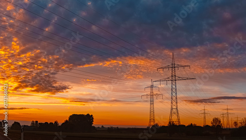 Sunset with a dramatic sky and overland high voltage lines soon to be replaced by Ostbayernachse and tree silhouettes near Wisselsing, Osterhofen, Deggendorf, Bavaria, Germany