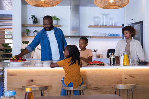 African American family gathering at kitchen island, father in denim reaching for apples