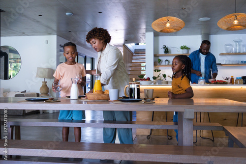 African American family gathering around dining table in kitchen reaching carafe of orange juice
