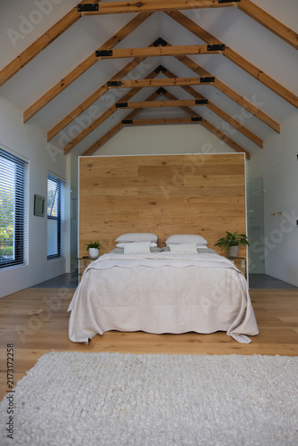 Minimalist bedroom featuring centered bed with tall wooden headboard, light bedding, potted plants