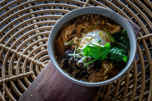 фотографія Freshly cooked Asian noodle soup topped with soft poached egg, green vegetables, and crispy shallots served in a bowl on a rattan table