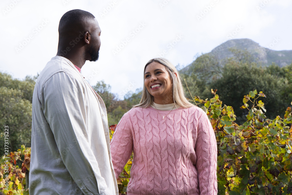 Fototapeta premium African American couple standing among grapevines, woman in pink sweater with pendant, man looking