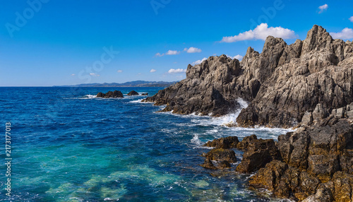 Rocky island shore with dark cliff formations surrounded by clear blue ocean water