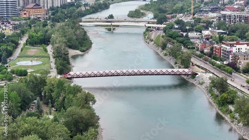 flying above Bow River next to Prince’s Island Park towards Peace Bridge and Bow River Pathway, with parts of Downtown Calgary ( Alberta, Canada) on left side - 4k aerial video footage 