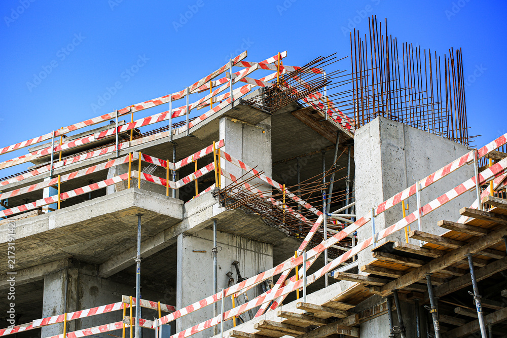 Obraz premium Construction site with reinforced concrete structure, rebar columns and striped safety barrier tape under clear sky, building renovation progress