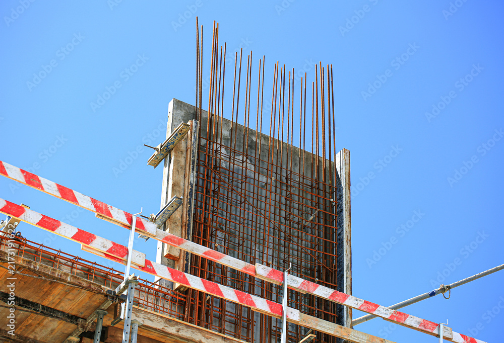 Naklejka premium Reinforced concrete wall with dense rebar mesh grid and wooden formwork at construction site, industrial building structure under clear sky closeup