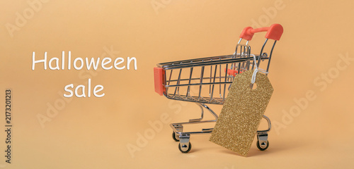Shopping cart with a glittery tag on an orange background, featuring the text 'Halloween sale', suggesting a festive shopping promotion.