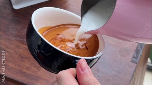 Barista Pouring Steamed Milk into Black Cup to Create Winged Heart Latte Art