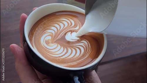Barista Pouring Steamed Milk into Black Cup to Create Winged Heart Latte Art