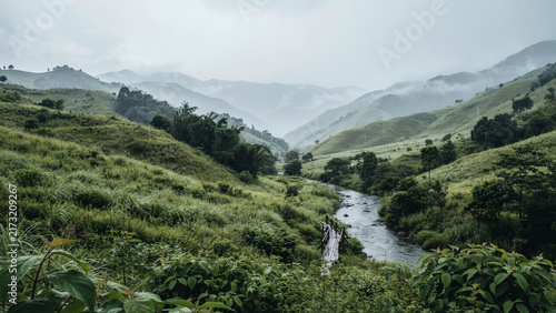 Green mountain valley landscape with winding stream and misty peaks