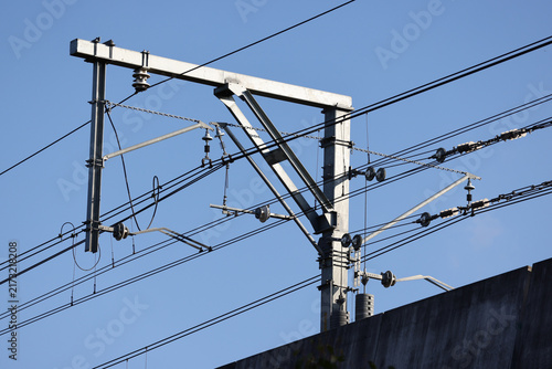 View of overhead railway electrification infrastructure with catenary wires and a steel support mast against a clear blue sky in Rouse Hill, New South Wales, Australia.