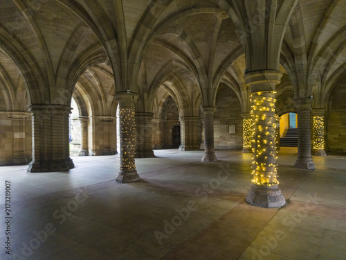 View of the stone vaulted cloisters at the University of Glasgow decorated with warm fairy lights on the columns in Glasgow, Scotland, United Kingdom.