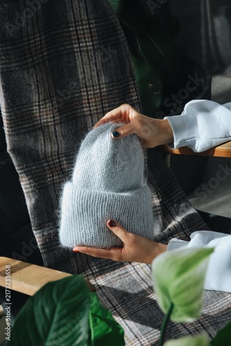 Foto Female hands holding warm fluffy handmade mohair beanie on cozy plaid blanket ba
