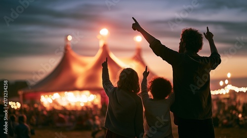 At sunset, a family's silhouettes point toward a brightly illuminated circus tent.