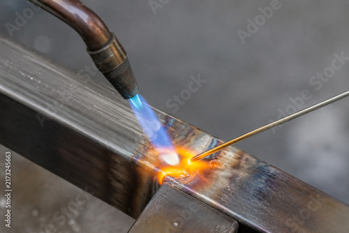 Close-up of a blue torch flame heating a metal joint with molten filler metal.
