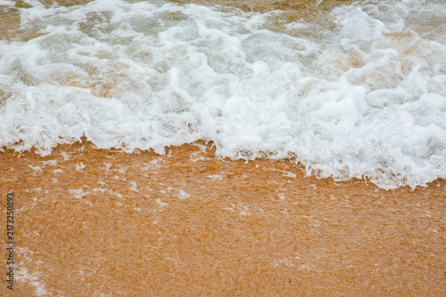 Fotografie Sea foam washing onto a sandy beach in Vietnam, creating a natural pattern of white bubbles against warm golden sand