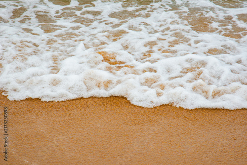 Fotografie Sea foam washing onto a sandy beach in Vietnam, creating a natural pattern of white bubbles against warm golden sand