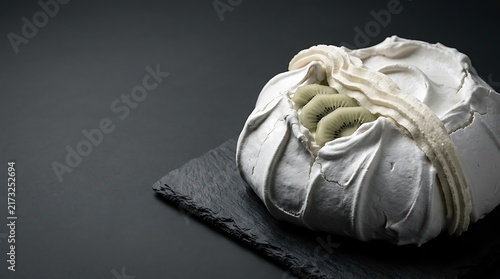 Classic zealand pavlova featuring a light crisp meringue base topped with fluffy whipped cream and fresh sliced kiwi fruit served on a dark slate platter plate.