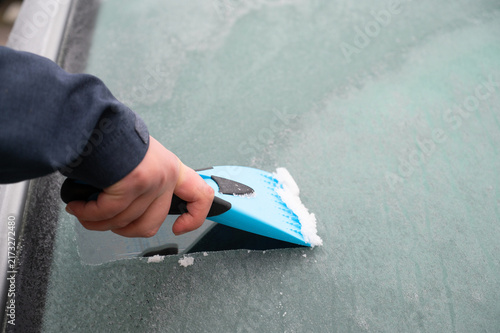 Driver is removing snow from car windshield with ice scraper and broom, clean car window from icy frost, winter season